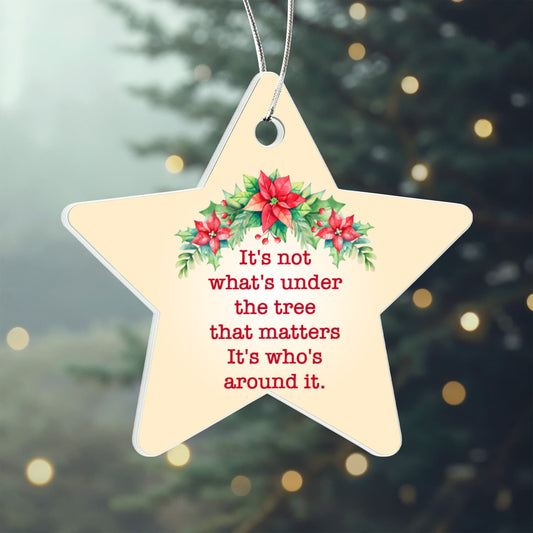 Star-shaped Christmas ornament with poinsettias and a quote against a blurred Christmas tree background.